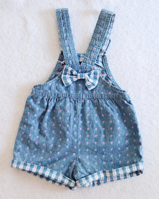 Vintage OshKosh B'Gosh girls light blue denim floral shortall, front flat lay, ditsy pink floral print, gingham-lined cuffed hem, pink OshKosh patch