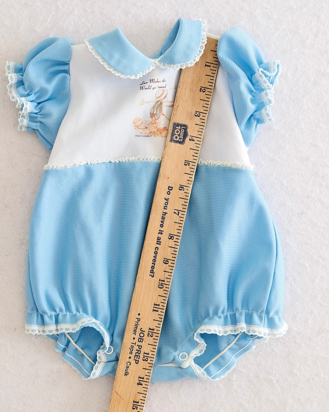 Vintage Holly Hobbie girls light blue white bubble romper, front flat lay, Holly Hobbie graphic on white bib, lace-trimmed flutter sleeves, Peter Pan collar, lace hem, snap bottom closure