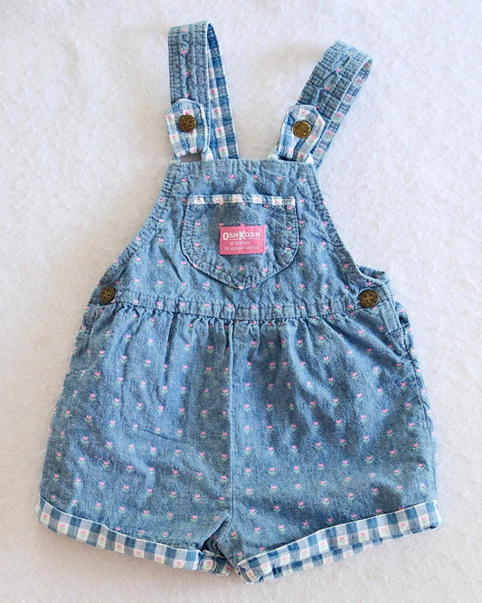 Vintage OshKosh B'Gosh girls light blue denim floral shortall, front flat lay, ditsy pink floral print, gingham-lined cuffed hem, pink OshKosh patch