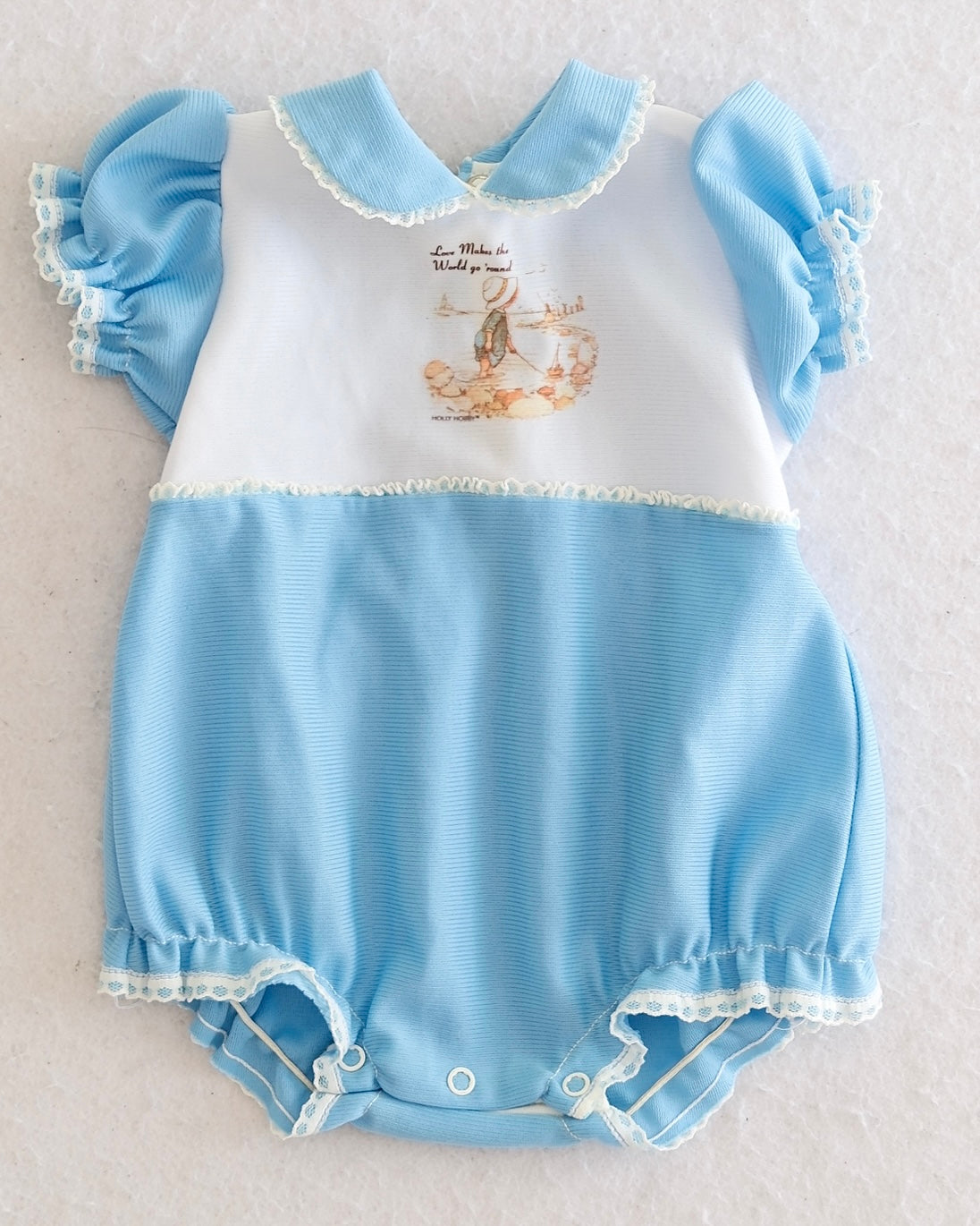 Vintage Holly Hobbie girls light blue white bubble romper, front flat lay, Holly Hobbie graphic on white bib, lace-trimmed flutter sleeves, Peter Pan collar, lace hem, snap bottom closure