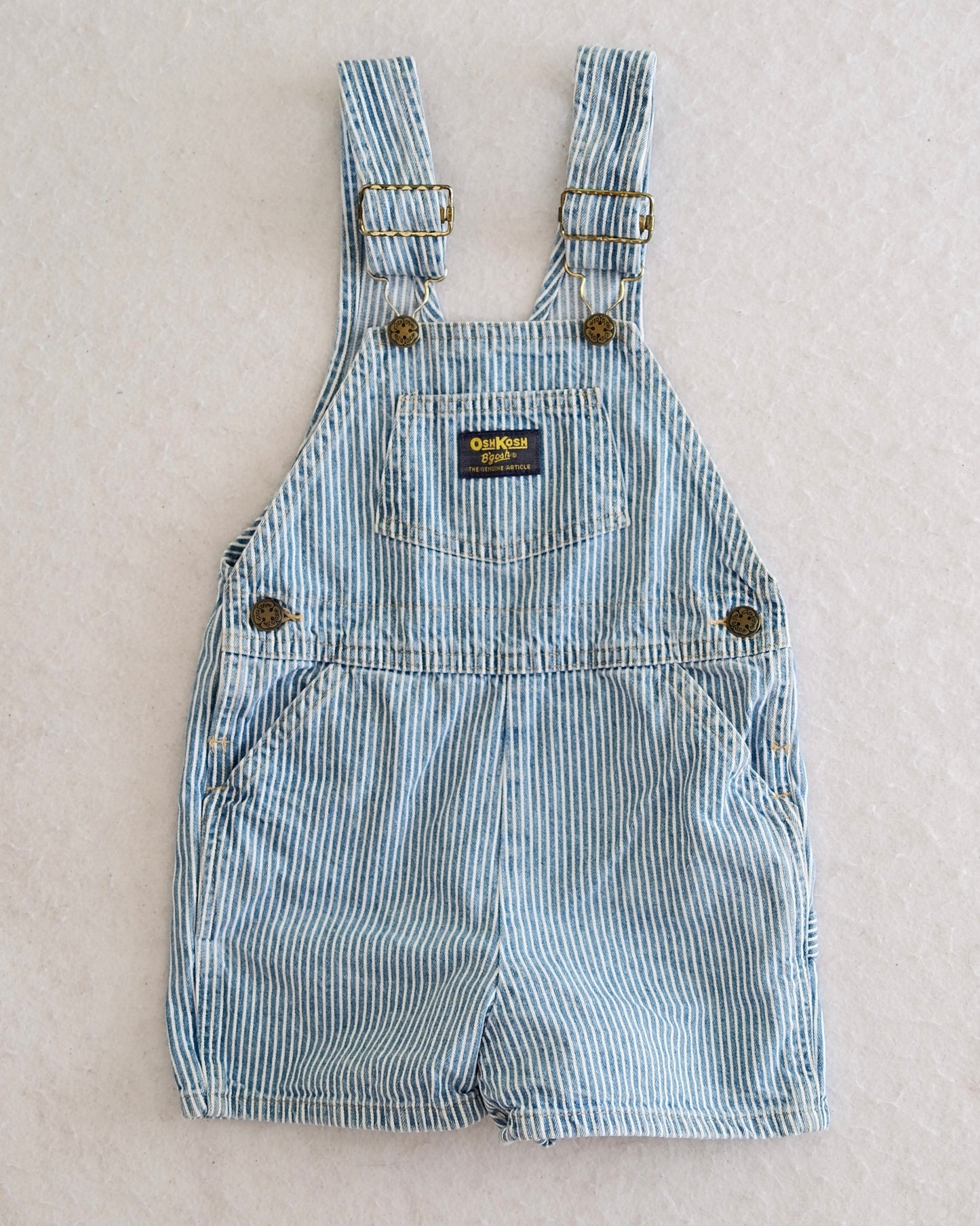 Vintage OshKosh B'Gosh kids blue and white hickory stripe shortalls size 4T, front flat lay, bib front pocket with navy OshKosh label, 