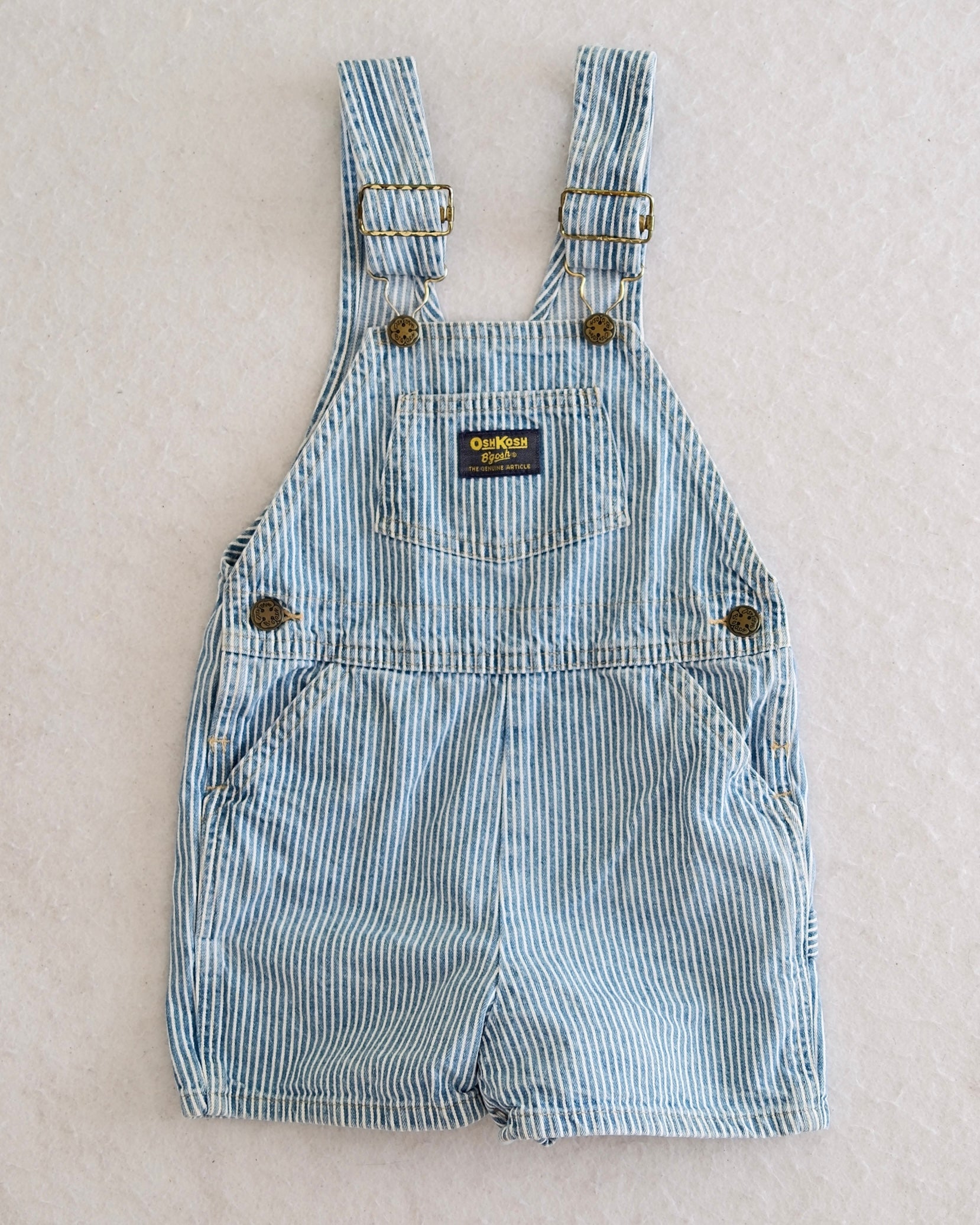 Vintage OshKosh B'Gosh kids blue and white hickory stripe shortalls size 4T, front flat lay, bib front pocket with navy OshKosh label, 