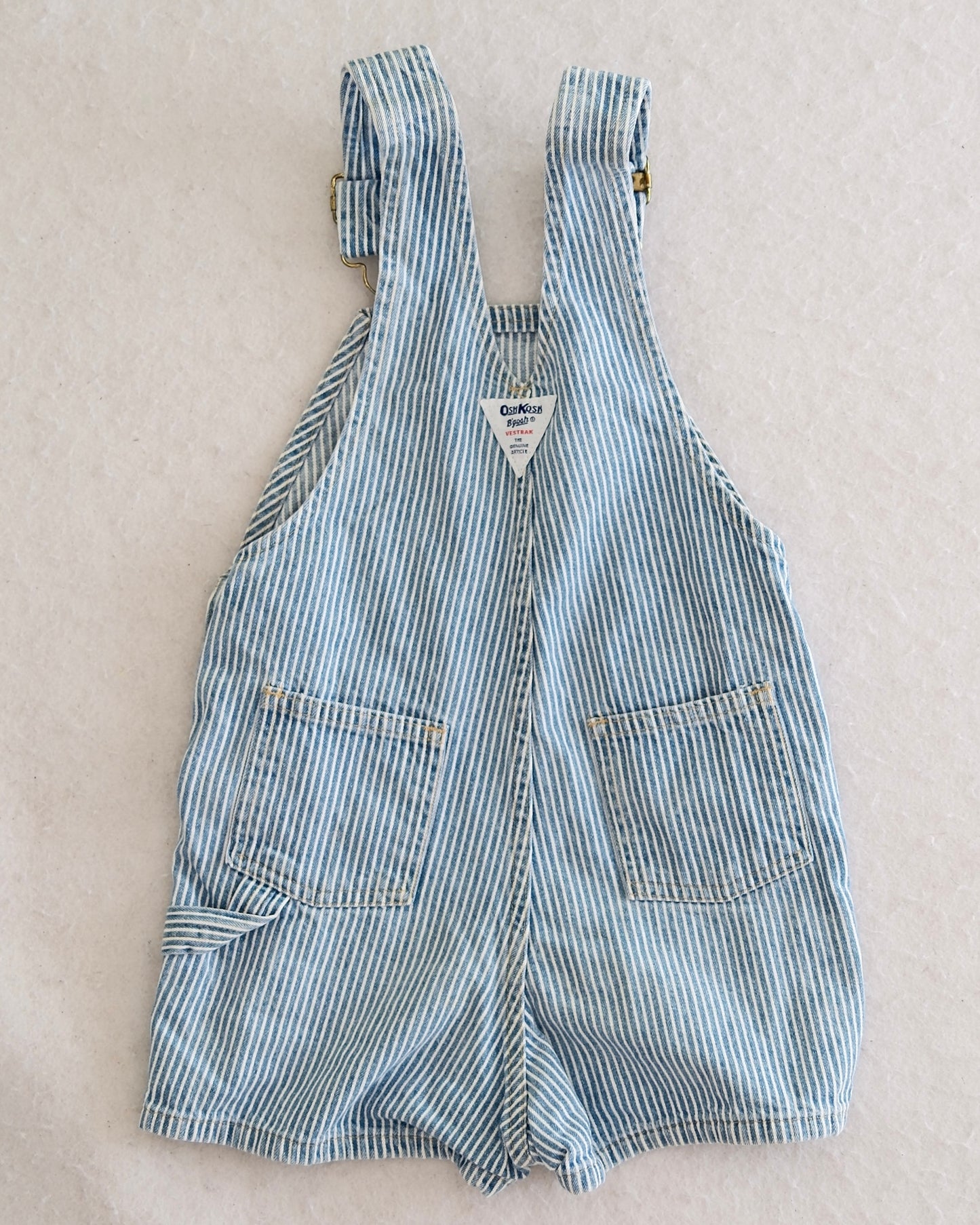Vintage OshKosh B'Gosh kids blue and white hickory stripe shortalls size 4T, front flat lay, bib front pocket with navy OshKosh label, 