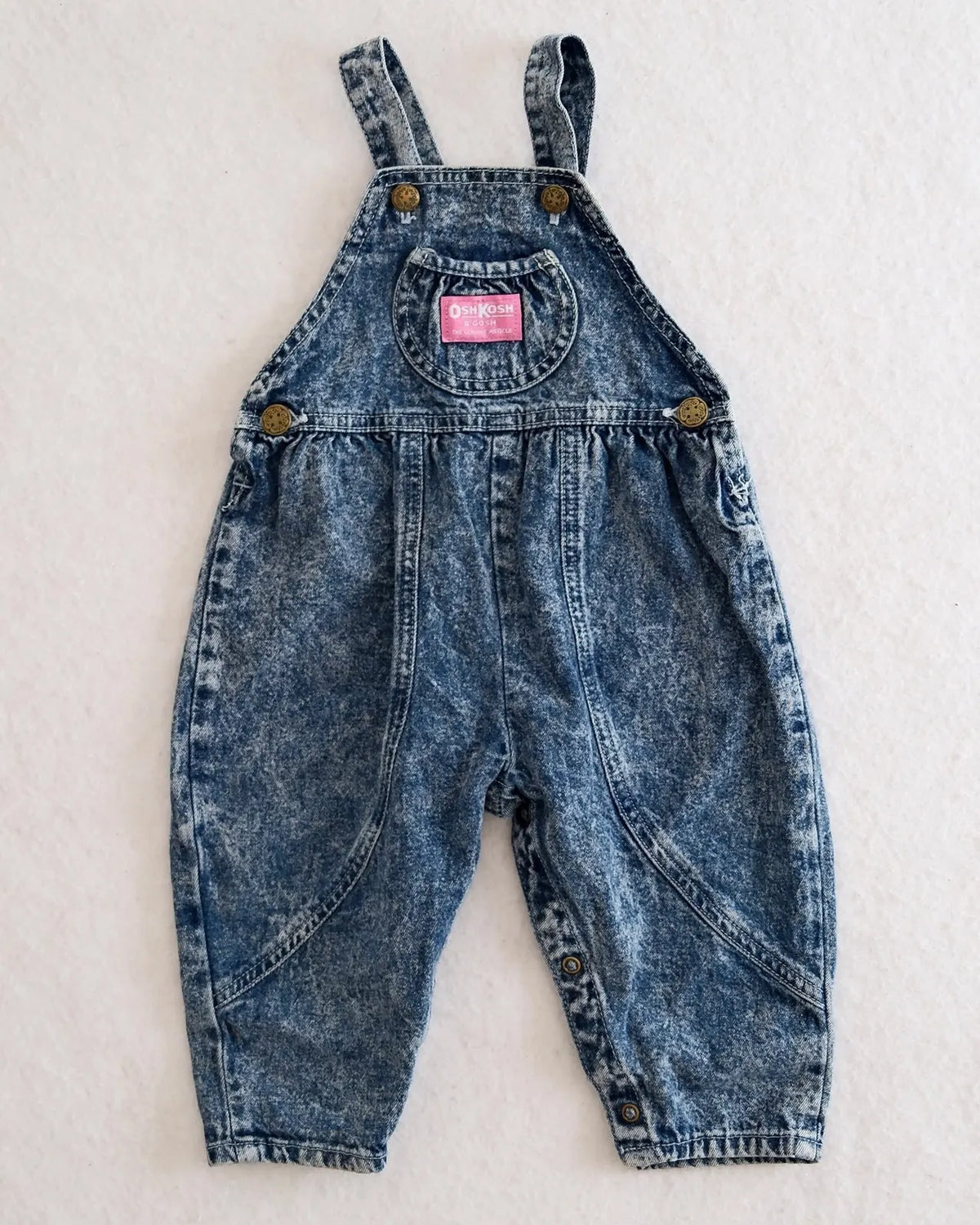 Vintage OshKosh B'gosh blue acid wash overalls with pink label and embossed OshKosh girl on back